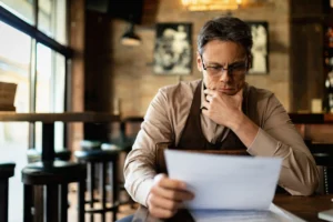 Pensive Cafe Owner Reading Going Through Paperwork Reading Reports After Working Hours 11zon 11zon - ERJ Assessoria Contábil e Tributaria